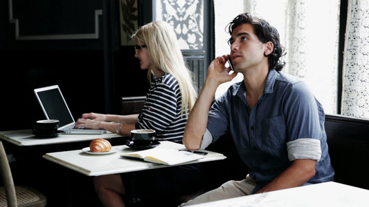 男人在咖啡馆里用手机，女人在咖啡馆里用笔记本电脑视频