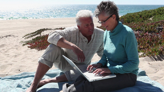 一对夫妇在沙滩上看笔记本电脑视频