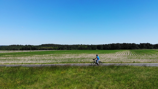空中无法辨认的人骑着绿色电动自行车沿着一条穿过大草地视频
