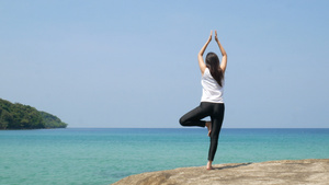 4K一个女人在暑假期间在海边的一块岩石上练习瑜伽时站13秒视频