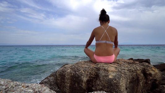 美丽的女人在沙滩上练习瑜伽冥想坐在石头上视频