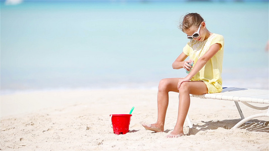 戴着帽子的小女孩在热带沙滩上坐着一瓶防晒霜视频