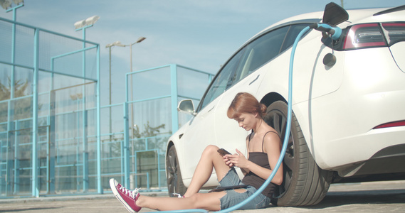 女孩在她的电动汽车充电时在地面上等待着视频