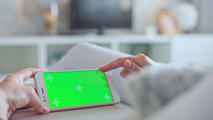 身穿白色牛仔裤的年轻妇女躺在沙发上用绿色屏幕使用智能手机46秒视频