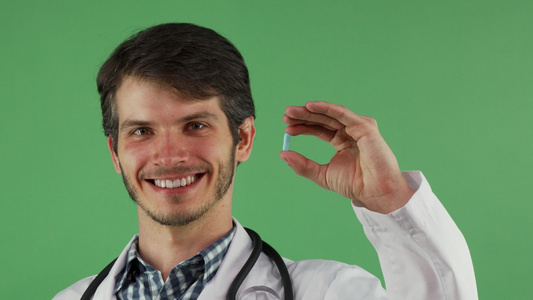 快乐的男医生笑着带着蓝药片在绿色背景下视频