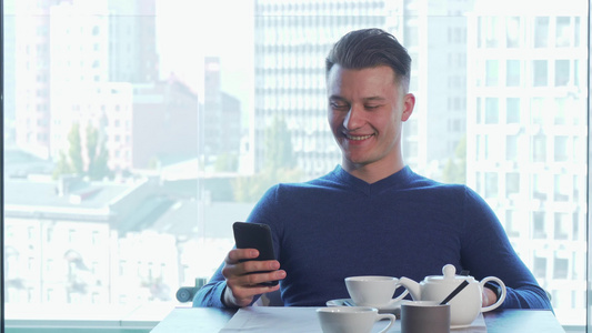 快乐的英俊男人笑得开心使用他的智能电话喝茶视频