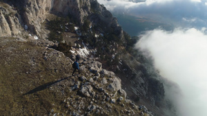 有背包的徒步男子正在行走站在云层上方山顶的陡峭边缘15秒视频