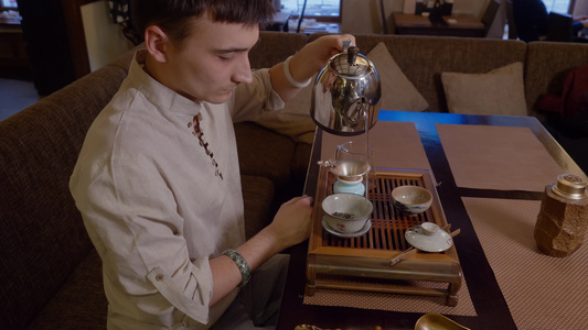 在传统仪式举行时用干茶在碗中的水壶里倒热水的男子视频