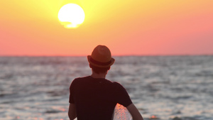 一个戴着充气环的帽子的男人在海边看日落的剪影男性旅行者12秒视频