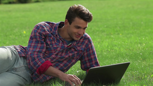 男人用笔记本电脑躺在公园的草地上视频