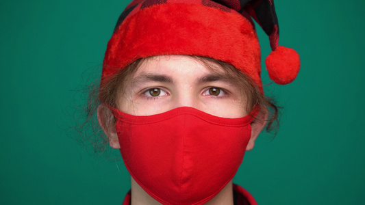 穿着圣塔帽男孩的肖像戴着红色医疗面具看着摄像机视频