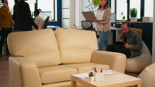 雇员在休息区使用手提笔记本电脑坐在可舒适沙发上打Pc视频