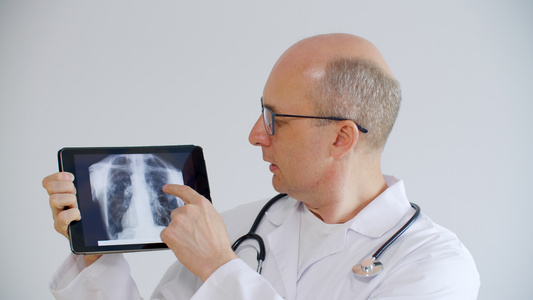 秃头医生在远程咨询时在平板电脑屏幕上显示肺部x射线视频