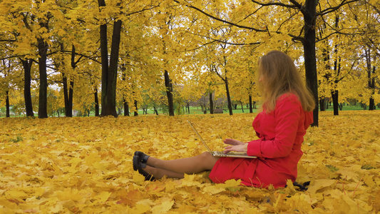 穿着红色斗篷长发的白人年轻女性在秋天坐在公园黄色地图视频