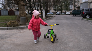幼儿女孩在街上走着三轮车旁边慢动作15秒视频