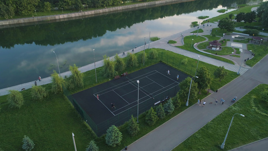 飞越在绿色城市公园的球场上打网球的球员人们走在人行道视频