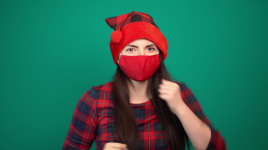 快乐的年轻女子穿着红色医疗面具在圣诞节圣塔帽舞视频