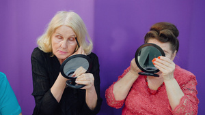 老妇人在美容学校的脸前小镜子上化妆两个成熟的女人在18秒视频
