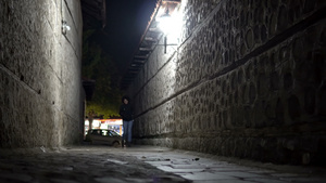 妇女穿着牛仔裤和靴子晚上在黑暗的城市小巷中走过14秒视频
