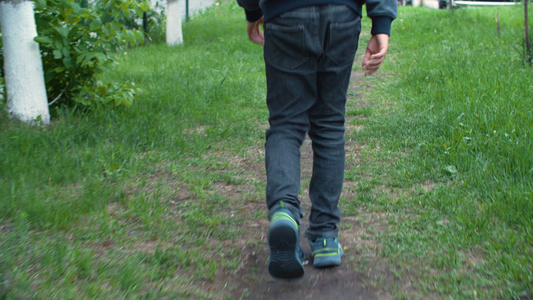 在夏季城市绿色草坪上的草地上行走的运动鞋的少年男孩视频