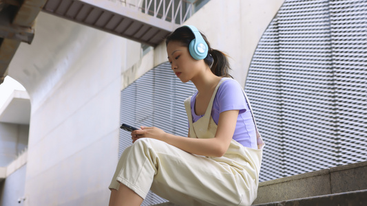 年轻女孩坐在台阶上用手机播放音乐视频