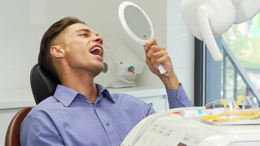 英俊的年轻人在牙科诊所的镜子里检查他的牙齿视频