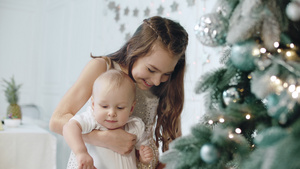 特写幸福女孩抱着孩子在现代住宅的圣诞树旁26秒视频