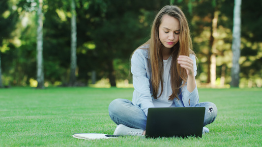 重点妇女利用笔记本在夏季公园的绿色草地上在线工作视频