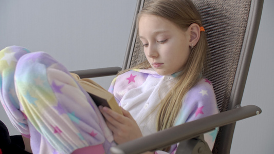 穿着睡衣在椅子上看书的专注的少女。穿着家居服的年轻女学生坐在家里的椅子上看书视频