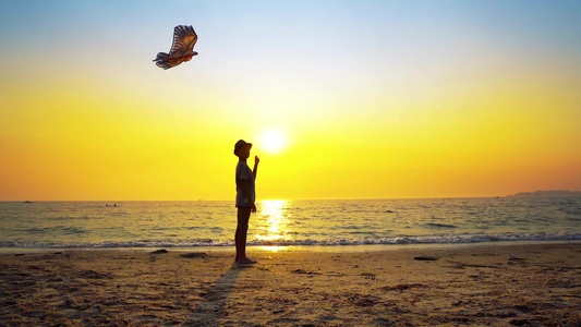 男孩在暑假日落的空沙滩上玩着帽子风筝视频