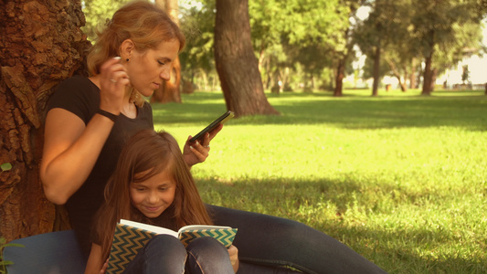 母亲和女儿坐在树旁,与她的女儿坐在一起视频