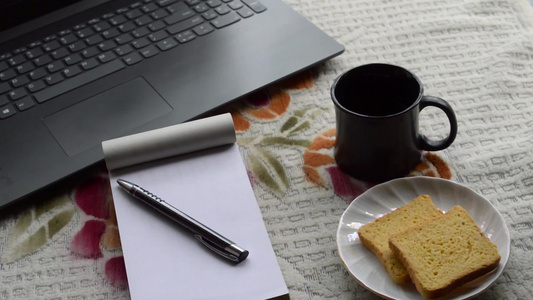 早餐咖啡在早晨的阳光下与笔记本电脑黑色笔和白色规则纸笔记本视频