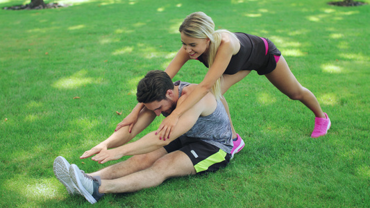 女运动教练员帮助健身男子在夏季公园伸腿视频