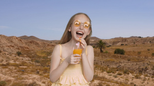 兴奋的女孩带着橙汁玻璃在沙漠和山脉的背景上大笑14秒视频