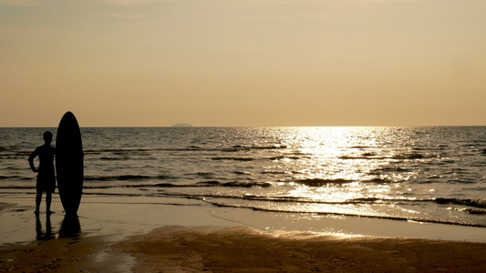 4K。冲浪者的剪影站在海滩上，日落时在热带海滩上放着长长的冲浪板，复古的色彩风格视频