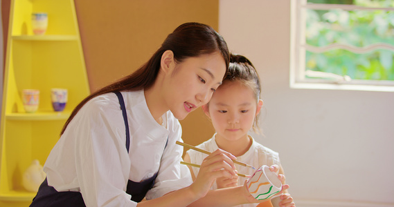 和蔼的青年老师教小女孩制陶画胚视频