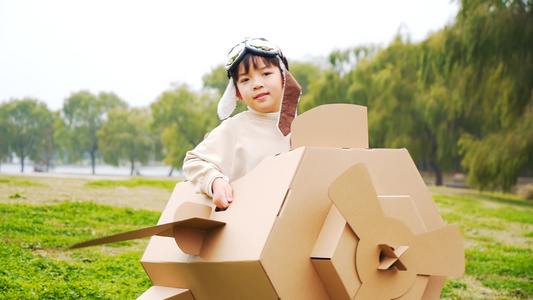 秋季公园草地上玩纸盒飞机的小男孩升格视频视频