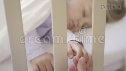 父母握着睡在婴儿床上的小孩子的手。 幸福的家庭和她的新生儿在一起。 这就是视频