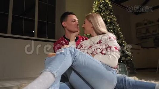 一对幸福的夫妇在家中的圣诞树附近的地板上玩得很开心，他们亲吻。视频
