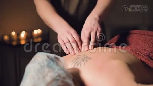 年轻的男性按摩治疗师正在按摩房间里的一个纹身的女人的背部做手指按摩，的灯光视频