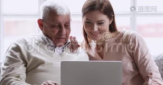微笑着年轻的成年孙女用笔记本电脑教老爷爷视频