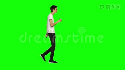 高大瘦小的年轻人平静地走着，在绿色的屏幕背景下喝着咖啡。 铬钥匙，4k射击。 侧写视图。视频