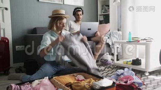 沙发上有笔记本电脑的人和戴帽子的女孩把衣服放进手提箱，准备旅行视频