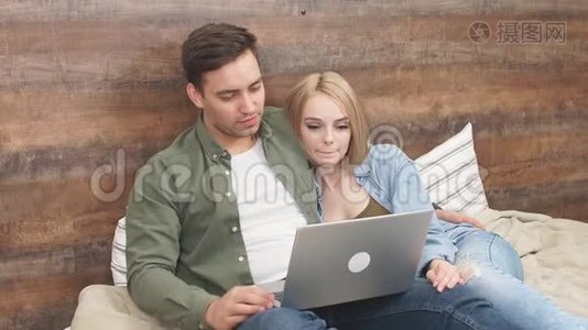 迷人的年轻夫妇在床上放松，在笔记本电脑上观看一段有趣的视频视频