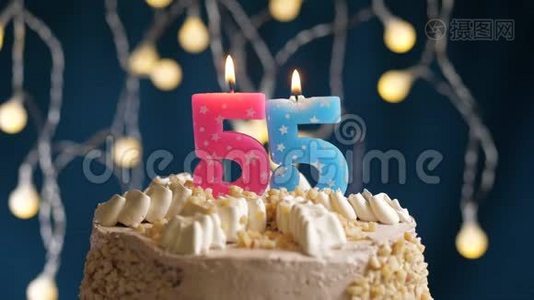 生日蛋糕，蓝色背景上有55个数字的粉红色燃烧蜡烛。 蜡烛吹灭了。 慢速运动和特写镜头视频