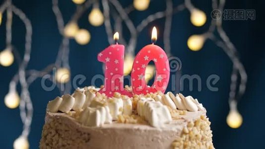 生日蛋糕，蓝色背景上有10个数字的粉红色燃烧蜡烛。 蜡烛吹灭了。 慢速运动和特写镜头视频