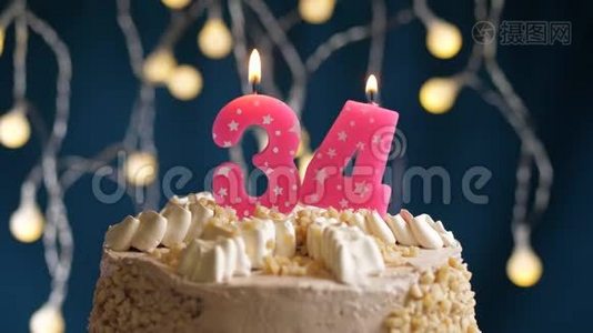 生日蛋糕，蓝色背景上有34个数字的粉红色燃烧蜡烛。 蜡烛吹灭了。 慢速运动和特写镜头视频