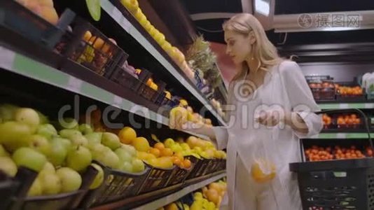 超市里一个漂亮的金发女郎选择橘子，把它们放进一个袋子里称重视频