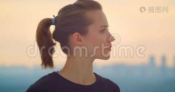 穿着黑色T恤的年轻漂亮运动女性慢跑者的特写照片，看着户外美丽的日落视频