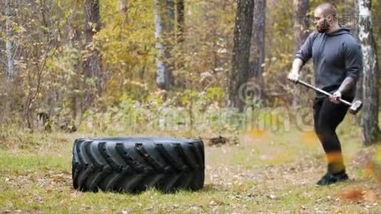 一名纹身男健美运动员用金属锤击卡车轮胎-秋天的森林视频
